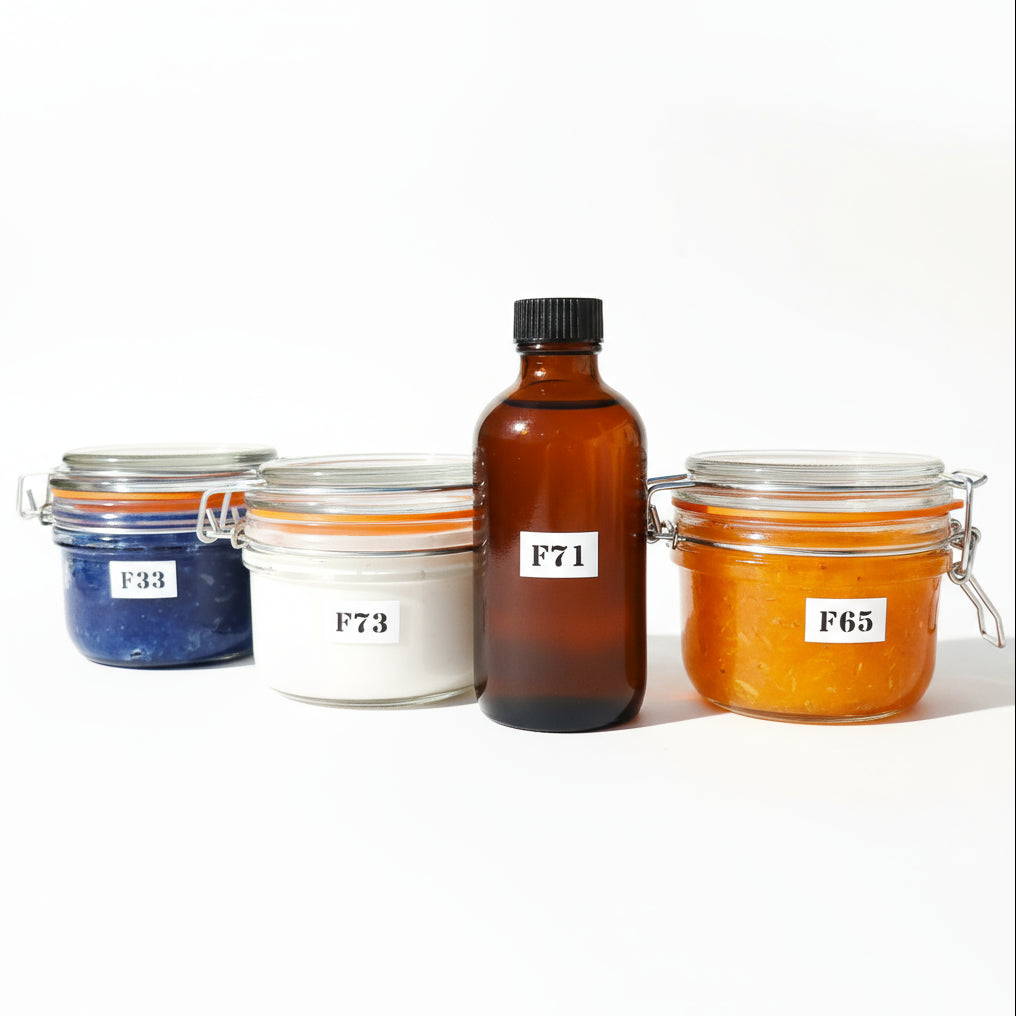 Four glass jars labeled F78, F71, F73, F76, arranged on a table with a background of flowers, indicating a spa therapy pack with different treatments possibly including a face and body exfoliator, a hydrating body cream, a soothing bath additive, and a skin firming serum.