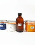 Four glass jars labeled F78, F71, F73, F76, arranged on a table with a background of flowers, indicating a spa therapy pack with different treatments possibly including a face and body exfoliator, a hydrating body cream, a soothing bath additive, and a skin firming serum.