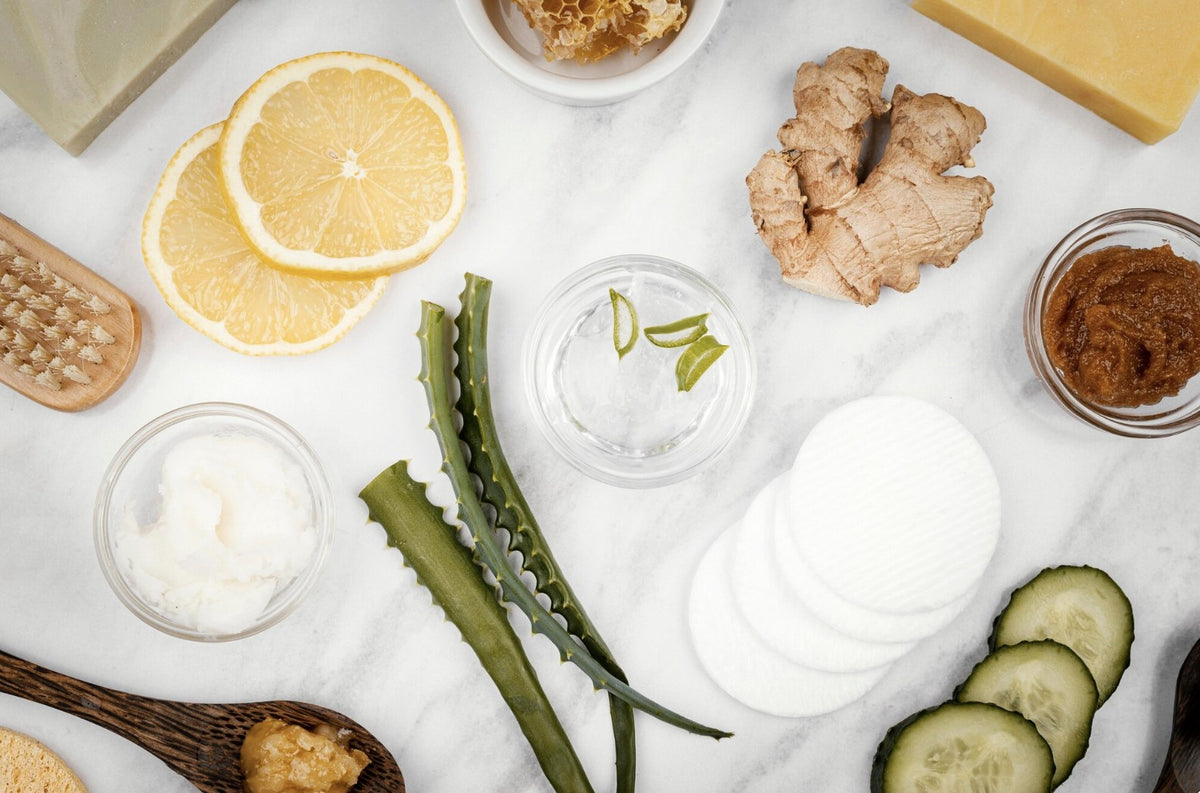 Fresh botanical ingredients laid out on marble, including aloe, ginger, cucumber and honey