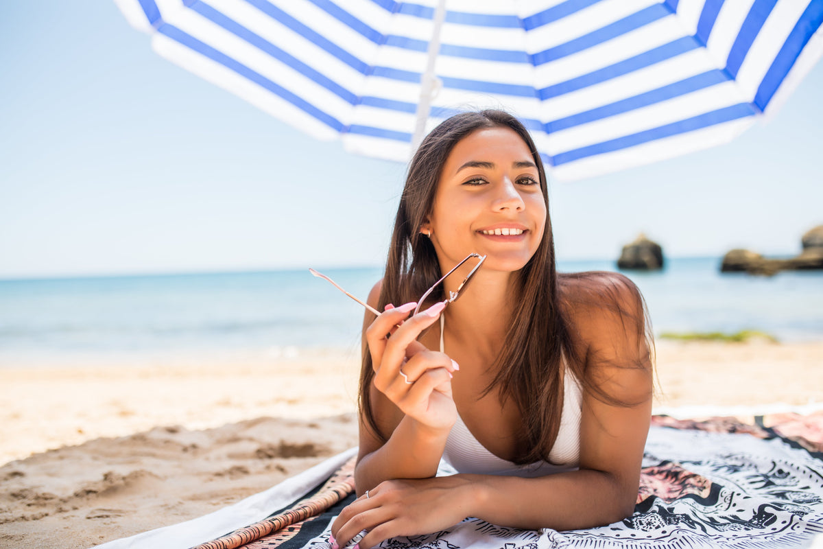 Woman resting in the shade of a beach umbrella, managing sun exposure with shade rather than daily sunscreen