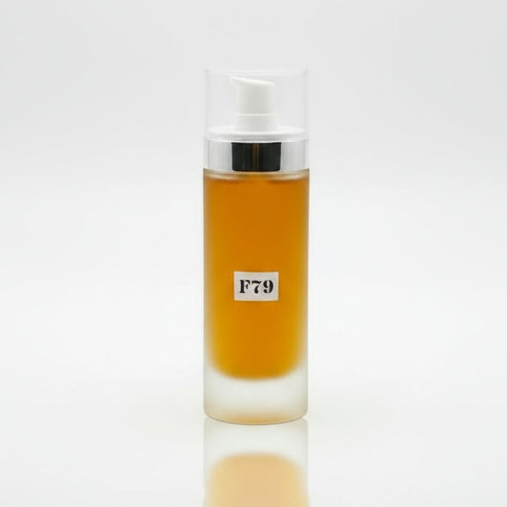 A clear glass bottle with a pump dispenser containing yellow liquid, labeled F79, placed on a wooden surface with floral background.