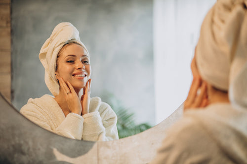 Woman in bathroom, looking at herself in the mirror admiring her natural glowing complexion after using Formula Flawless Skin Serum