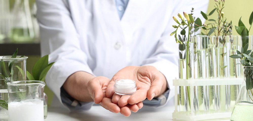 Lab Scientist showing one of our natural skincare formulations surrounded by lab equipment. 